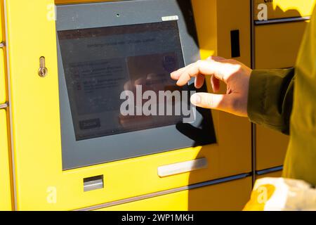 Augusta, Baviera, Germania - 25 febbraio 2024: Un uomo gestisce una stazione DHL per inviare un pacco o un pacco *** Ein Mann bedient eine DHL Packstation um ein Paket oder Päkchen zu verschicken Foto Stock