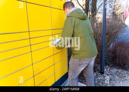 Augsburg, Baviera, Germania - 25 febbraio 2024: Un uomo rispedisce un pacco con ritorno Zalando utilizzando una Packstation DHL *** Ein Mann schickt ein Paket mit einer Zalando Retoure mit einer DHL Packstation Zurück Foto Stock