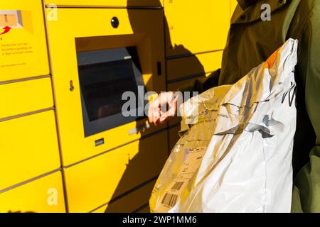 Augsburg, Baviera, Germania - 25 febbraio 2024: Un uomo rispedisce un pacco con ritorno Zalando utilizzando una Packstation DHL *** Ein Mann schickt ein Paket mit einer Zalando Retoure mit einer DHL Packstation Zurück Foto Stock