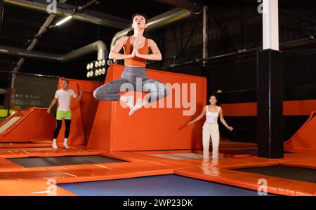 Donna di mezza età felice che pratica e salta sui trampolini in un centro sportivo al coperto, allenamento e moderno concetto di intrattenimento Foto Stock