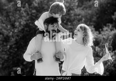 Papà mamma e bambino giocano insieme all'aperto. Figlio felice che mostra ai suoi genitori un aereo di carta. Famiglia felice e amorevole. Famiglia felice in vacanza. Foto Stock