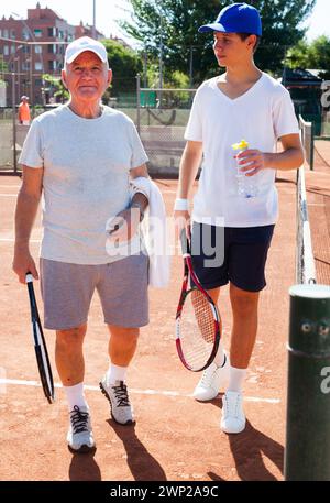 Uomo anziano e giovane che parlano sul campo giocando a tennis Foto Stock