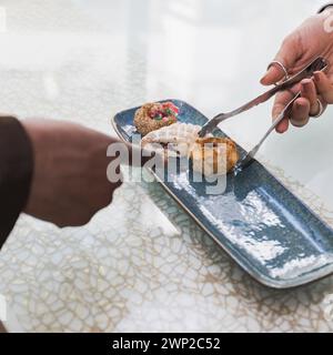 Foto ravvicinata della mano di un cliente che indica una pasticceria scelta, mentre il server la prepara per servire. Concetto di cibo e cultura. Foto Stock