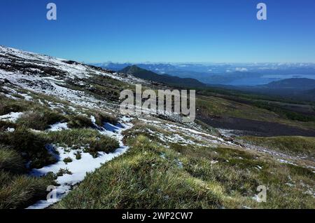 Paesaggio naturale, erba e neve sul versante montuoso del vulcano Villarrica, cielo azzurro cristallino, parco nazionale di Villarrica in Cile Foto Stock