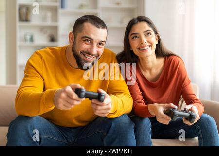 Giovane coppia felice che gioca ai videogiochi con i joystick a casa Foto Stock