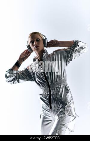 accattivante e bizzarro modello femminile con cuffie che indossano un abbigliamento robotizzato argentato e si godono la musica Foto Stock