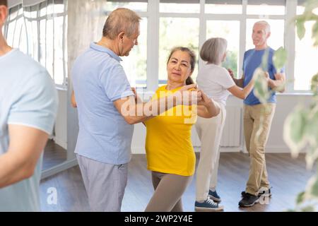Donna anziana e uomo positivi che praticano la danza del tango si muove in coppia durante una festa di gruppo in studio di danza Foto Stock