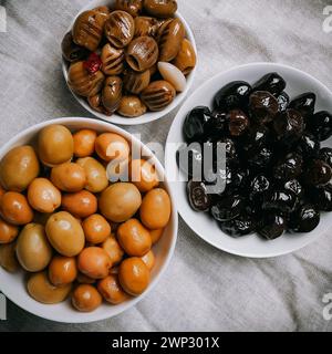 un set di tre tipi di olive in ciotole bianche su un tovagliolo grigio: olive verdi intere, olive nere, olive verdi grigliate in olio, snocciolate, vista dall'alto Foto Stock