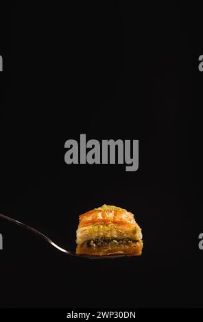 un delizioso baklava al miele con pistacchi su una forchetta su sfondo nero, vista laterale, copyspace Foto Stock