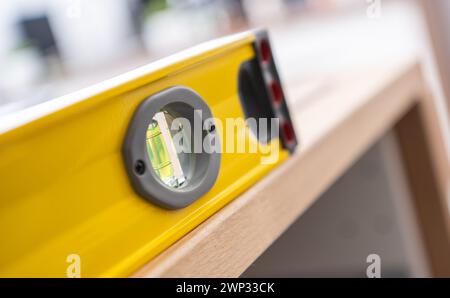 Livella a bolla d'acqua professionale gialla su un piano di legno. Tema di assemblaggio dei mobili. Foto Stock