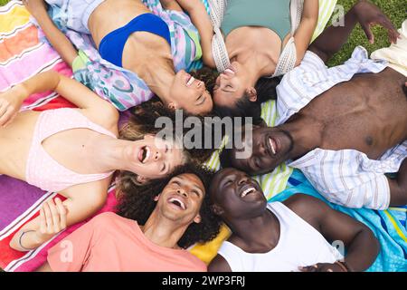 Diversi gruppi di amici ridono insieme mentre sdraiati su una coperta colorata all'aperto Foto Stock