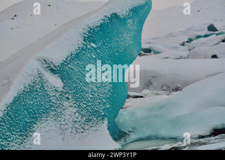 Un vivace iceberg blu immerso in un paesaggio innevato, che mostra la bellezza ghiacciata della natura. Ubicazione: Jokulsarlon Glacier Lagoon Islanda. Foto Stock