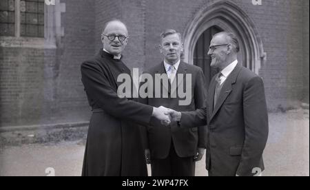 Anni '1950, storico, un ecclesiastico inglese, reverendo A. S Wye, fuori dal vicarage salutando i suoi nuovi guardiani, Oxford, Inghilterra, Regno Unito. Il XIII secolo vide apparire dei guardiani, membri di una congregazione eletti da e tra i parrocchiani, per rappresentare quelli di una fede religiosa, i laici e assumersi la responsabilità del tessuto della chiesa, dell'amministrazione e di altri doveri. Foto Stock