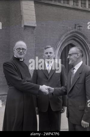 Anni '1950, storico, un ecclesiastico inglese, reverendo A. S Wye, fuori dal vicarage salutando i suoi nuovi guardiani, Oxford, Inghilterra, Regno Unito. Il XIII secolo vide apparire dei guardiani, membri di una congregazione eletti da e tra i parrocchiani, per rappresentare quelli di una fede religiosa, i laici e assumersi la responsabilità del tessuto della chiesa, dell'amministrazione e di altri doveri. Foto Stock