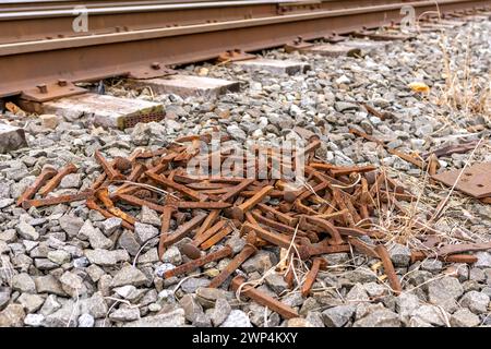 Mucchio di chiodi arrugginiti su pietra schiacciata accanto ai binari ferroviari. Foto Stock