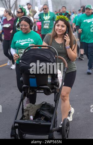 Folla di persone con magliette verdi, una donna al cellulare che spinge un carrozzino, durante St. Patrick's Day Run & Walk, Pharr, Texas, Stati Uniti. Foto Stock