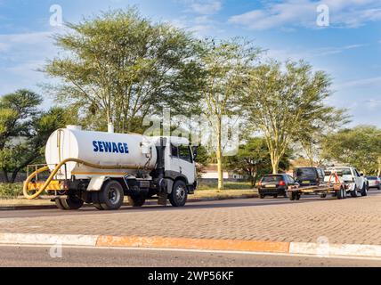 camion per acque reflue su strada in corrispondenza di un incrocio che guida dietro poche auto e un rimorchio Foto Stock