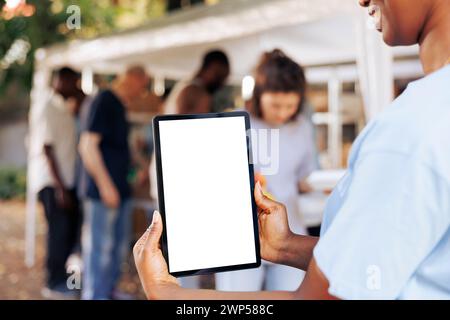 Una giovane donna nera ha un tablet intelligente con un modello di mockup isolato per messaggi di beneficenza. Volontaria afroamericana che afferra un gadget digitale con uno schermo bianco vuoto. Foto Stock
