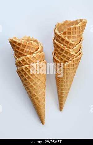 Due coni croccanti dorati per waffle si stagliano in posizione verticale su un semplice sfondo bianco, pronti per essere riempiti con un delizioso gelato Foto Stock