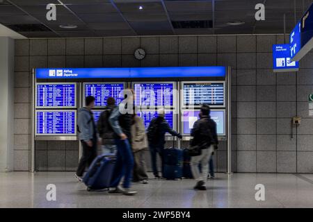 Aeroporto di Francoforte, Germania - 19 febbraio 2024: Le persone in movimento si sfocano in piedi e camminano di fronte a un tabellone di partenza Foto Stock