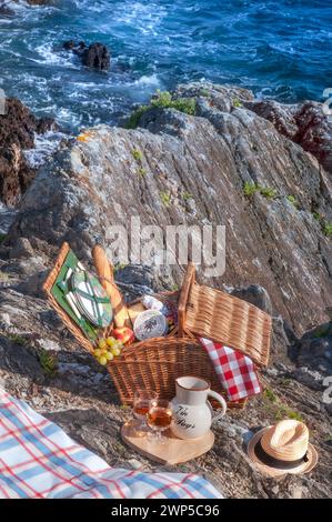 Cesto di vimini da picnic DELLA BRETAGNA con baguette, formaggio, frutta, salame e vino rosato tipici della costa francese. Doëlan Finistere Brittany Francia Foto Stock