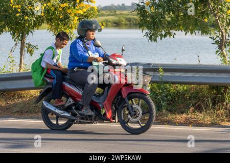 SAMUT PRAKAN, THAILANDIA, DEC 15 2023, Una donna cavalca un ragazzo in uniforme scolastica su una moto. Foto Stock