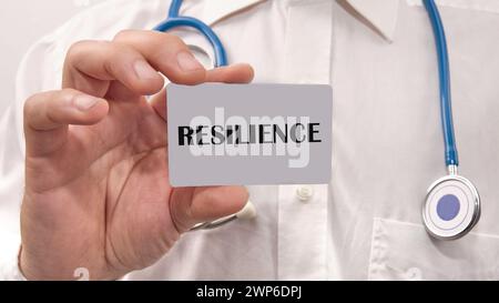 La parola scritta RESILIENZA sulla carta nella mano di un uomo con una camicia bianca Foto Stock