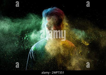 Uomo asiatico spruzzato con colorata polvere di holi e divertirsi isolato su sfondo nero. Color festival India. Foto Stock