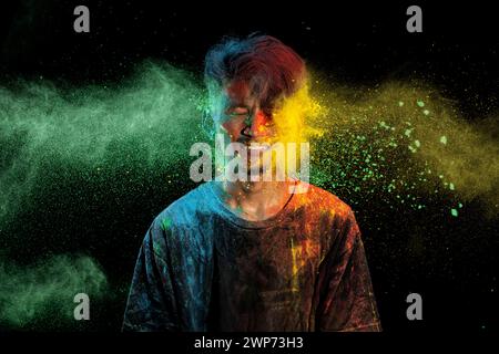 Uomo asiatico spruzzato con colorata polvere di holi e divertirsi isolato su sfondo nero. Color festival India. Foto Stock