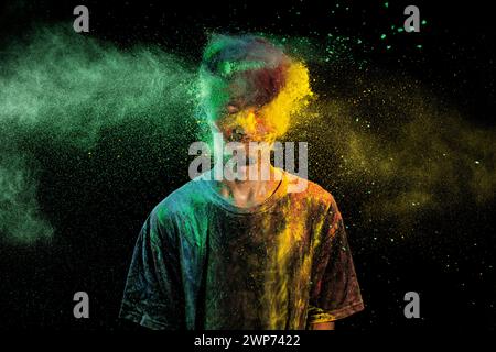 Uomo asiatico spruzzato con colorata polvere di holi e divertirsi isolato su sfondo nero. Color festival India. Foto Stock