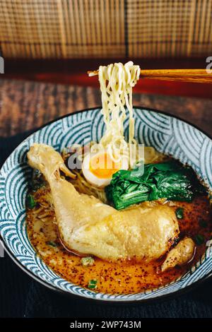 Una ciotola di zuppa con spaghetti e pollo. Il pollo viene cotto e l'uovo galleggia nella zuppa. La ciotola è blu e bianca Foto Stock
