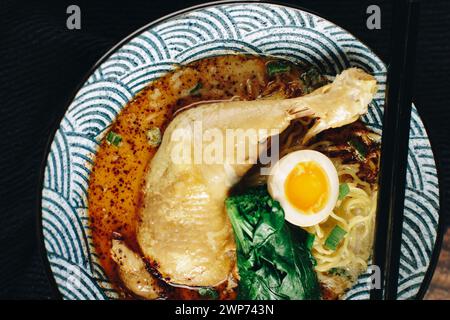 Una ciotola di zuppa con un pezzo di pollo e un uovo sopra. La zuppa è di colore ricco e cremoso e il pollo e l'uovo aggiungono un tocco di colore e consistenza a t Foto Stock