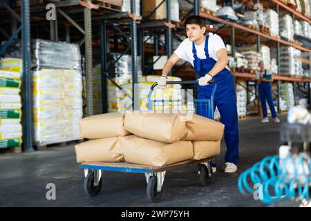 Il giovane tira il carrello con le borse in magazzino Foto Stock