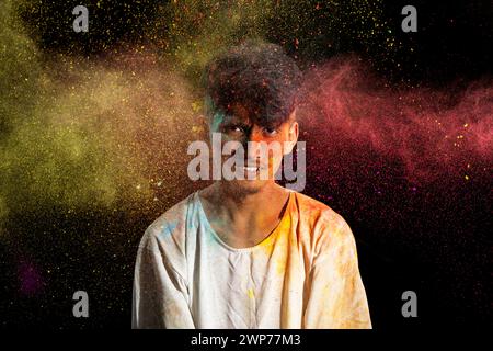 Uomo asiatico spruzzato con colorata polvere di holi e divertirsi isolato su sfondo nero. Color festival India. Foto Stock