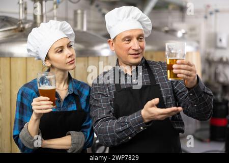 I produttori di birra interessati, maschi e femmine, che esaminano la qualità della birra in birrificio Foto Stock