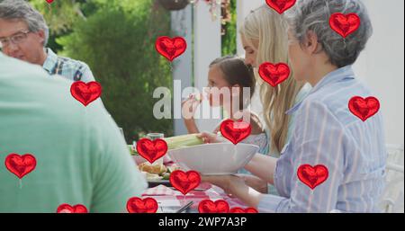Immagine di palloncini cardiaci sulla felice famiglia caucasica che mangiano insieme in giardino Foto Stock