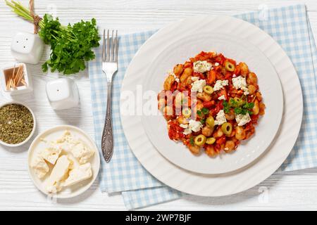 plaki gigantes, fagioli giganti greci al forno in una grossa salsa di pomodoro cosparsa di feta, olive e prezzemolo fresco sul piatto su un tavolo di legno bianco w. Foto Stock