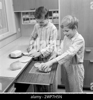 Colazione negli anni '1950 Due ragazzi sono in piedi in pigiama per preparare la colazione. Una fetta di pane sul tagliere e una spalma il burro sul panino. 1956. Conard rif. 3167 Foto Stock