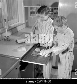 Colazione negli anni '1950 Due ragazzi sono in piedi in pigiama per preparare la colazione. Una fetta di pane sul tagliere e una spalma il burro sul panino. 1956. Conard rif. 3167 Foto Stock