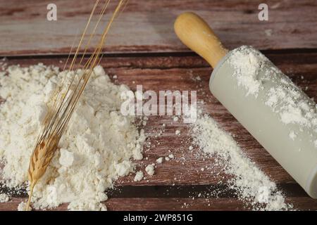 mucchio di farina con un'orecchia di grano sopra di essa, accanto a un mattarello, su un tavolo di legno e spazio per copiare Foto Stock