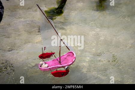 Il bambino gioca con un dhow giocattolo a vela realizzato con sandali di plastica sulla spiaggia di Jambiani, Zanzibar, Tanzania Foto Stock