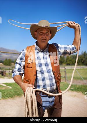 Cowboy, ranch e lazo all'aperto, sole e cinghie per wrangler e contadini del Texas a Stable. Uomo maturo, selvaggio West ed estate in agricoltura, cappello e.. Foto Stock