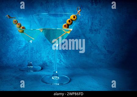 Martini. Due bicchieri di cocktail martini sporchi con vermouth e olive, aperitivo, su sfondo blu, vista laterale con spazio fotocopie Foto Stock