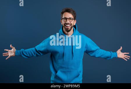 Allegro ragazzo in felpa con cappuccio blu che diffonde le braccia e sorride alla fotocamera Foto Stock