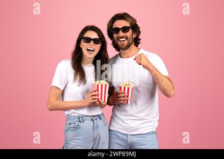 Allegra coppia in t-shirt bianche e occhiali da sole, ridendo e tenendo in mano scatole di popcorn a righe rosse e bianche Foto Stock