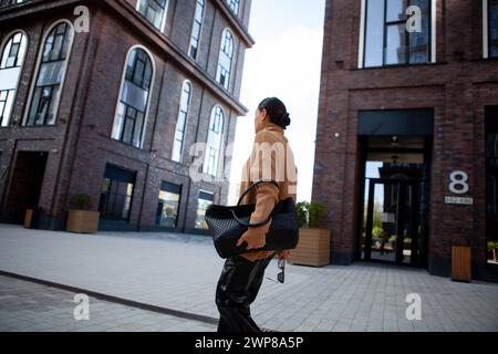 Foto di uno stile di vita di una donna in movimento, che cammina vicino agli edifici della città. Una scena urbana candida che cattura movimenti dinamici. Foto Stock