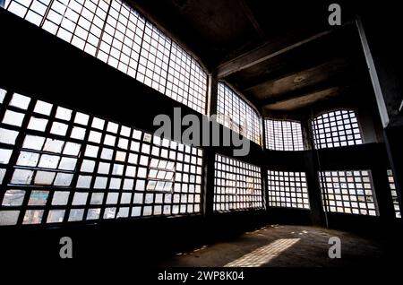 Una stanza vuota con numerose finestre all'interno di un edificio industriale abbandonato Foto Stock