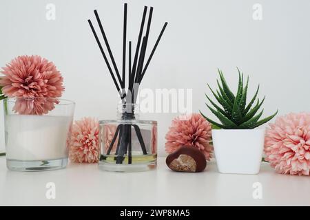 Composizione di fiori artificiali rosa, bastoncini di incenso in vaso di vetro con olio essenziale. Ancora la vita su un tavolo bianco. Fiore di aloe in una pentola bianca. RO Foto Stock