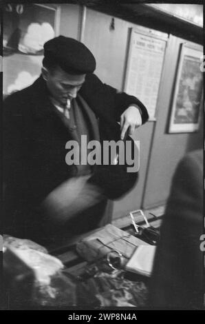 Una fotografia in bianco e nero del 1959 che mostra un viaggiatore sotto controllo bagagli alla stazione estera dell'aeroporto di Varsavia. L'immagine raffigura un controllo del passaporto e un briefing da parte del personale doganale nell'ambito delle procedure aeroportuali standard. Foto Stock