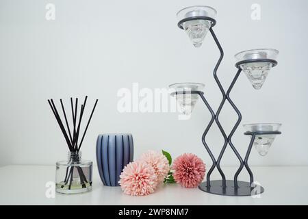 Composizione con bastoncini di incenso, olio essenziale in vaso di vetro e fiori artificiali di spugna rosa. Lampadario alto in metallo con supporti in vetro per piccole dimensioni Foto Stock